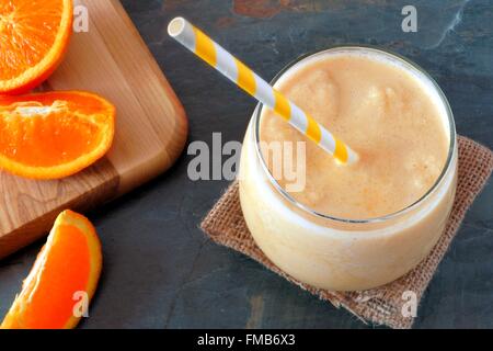 Gesunde orange Smoothie in ein Glas mit gestreiften Stroh und frischen Früchten Scheiben, nach unten gerichtete Blick auf Schiefer Stockfoto