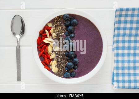 Nahrhafte smoothie Heidelbeere Schüssel mit Goji Beeren, Mandeln und Chia Samen auf weißem Holz mit Stoff und Löffel Stockfoto