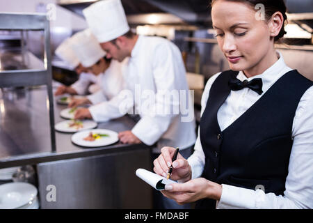 Kellnerin mit Notizen in der gewerblichen Küche Stockfoto