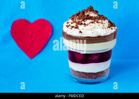 Romantische geschichtete Dessert mit zerbröselten Cookies an der Spitze in der Nähe ein Herz geformt rote Serviette auf einem hellblauen Hintergrund. Stockfoto