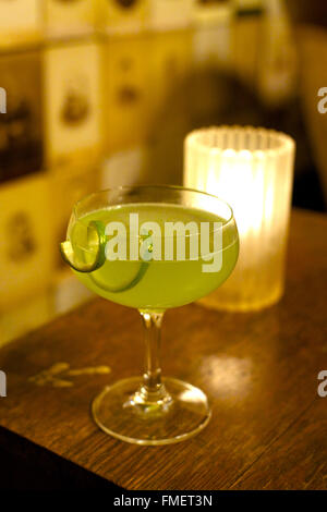 Ein grüner Cocktail sitzt auf einem hölzernen bar oben mit einer Kerze im Hintergrund. Stockfoto