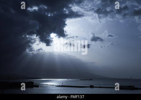 Sonnenlicht geht durch dunkle stürmischen Wolken. Bucht von Izmir, Türkei. Blau getönten stilisierte Foto Stockfoto