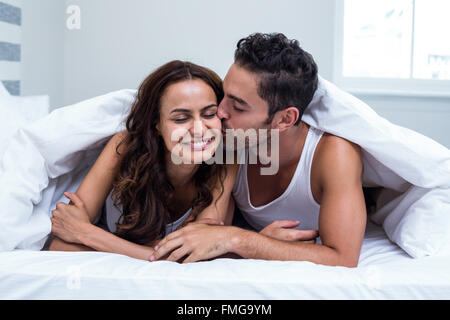 Lächelnder Mann küsst Frau liegend unter Decke Stockfoto
