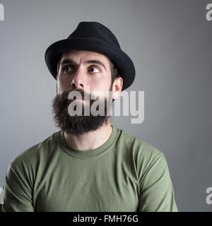 Verwirrt bärtigen Mann mit schwarzen Hut wegsehen. Kopfschuss Nahaufnahme Portrait über graue Studio-Hintergrund mit Vignette. Stockfoto