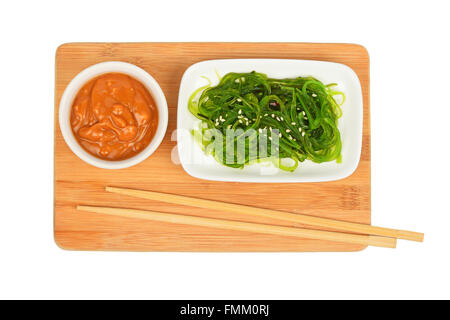 Teil des asiatischen grünen mariniertes Seegras Salat in kleinen weißen Teller mit Erdnuss-Sauce auf Bambus Holzbrett mit Stäbchen iso Stockfoto