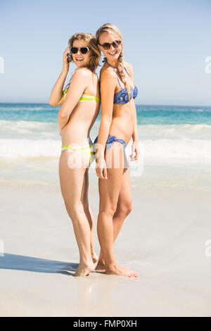 Zwei glückliche Frauen in Bikini und Sonnenbrille stehen Rücken an Rücken Stockfoto