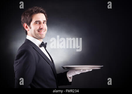 Porträt einer jungen Kellner hält eine leere Schüssel auf schwarzem Hintergrund Stockfoto