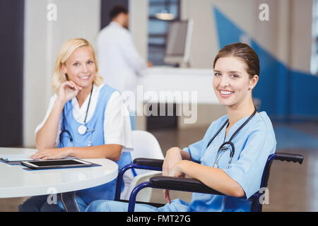 Porträt von lächelnden Ärztin auf Rollstuhl sitzend mit Kollegen Stockfoto