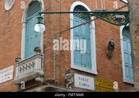 Straßenschilder auf die Ecke eines antiken venezianischen Gebäude, sowie mit einem Marmorbad und Balkon, ein Stein Engel und ein Wappen. Die Fenster sind mit grünen Fensterläden. Stockfoto