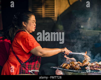 Luang Prabang, Luang Prabang, Laos. 13. März 2016. Eine Frau grillt Fleisch auf dem Markt in Luang Prabang. Luang Prabang wurde 1995 zum UNESCO-Weltkulturerbe ernannt. Der Umzug gespeichert koloniale Architektur der Stadt, aber die Explosion des Massentourismus hat ein Tribut an die Seele der Stadt. Laut einer aktuellen Studie geht jetzt ein kleines Grundstück, das für $8.000 vor drei Jahren verkauft für $120.000. Viele langjährige Bewohner sind Verkauf ihrer Häuser und Umzug in kleine Entwicklungen rund um die Stadt. Die alten Häuser sind dann in Thermen, Pensionen und Restaurants umgewandelt. Die Stadt ist berühmt für die m Stockfoto