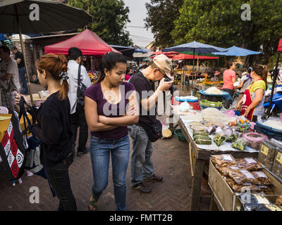 Luang Prabang, Luang Prabang, Laos. 13. März 2016. Ein Tourist fotografiert einen Nudel-Stand auf dem Markt in Luang Prabang während Shopper um ihn herum gehen. Luang Prabang wurde 1995 zum UNESCO-Weltkulturerbe ernannt. Der Umzug gespeichert koloniale Architektur der Stadt, aber die Explosion des Massentourismus hat ein Tribut an die Seele der Stadt. Laut einer aktuellen Studie geht jetzt ein kleines Grundstück, das für $8.000 vor drei Jahren verkauft für $120.000. Viele langjährige Bewohner sind Verkauf ihrer Häuser und Umzug in kleine Entwicklungen rund um die Stadt. Die alten Häuser sind dann in Pensionen, re umgewandelt. Stockfoto