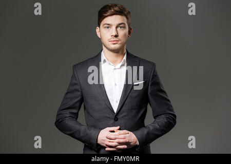 Porträt von Ernst zuversichtlich Jungunternehmer im schwarzen Anzug und weißem Hemd auf grauem Hintergrund Stockfoto