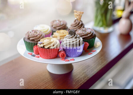 Acht köstlich süßen Muffins bedeckt mit Sahne Schokolade, Vanille und verschiedene andere Pfändungen neben wenig rosa er Stockfoto