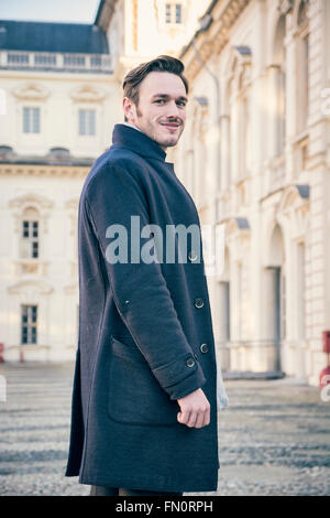 Taille, der stilvolle junge Mann tragen Fell und Looking Up vor historischen Gebäude im Hintergrund Stockfoto