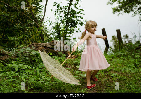 kleines blondes Mädchen mit weißen Sonnenschirm auf der grünen Wiese am Teich Stockfoto