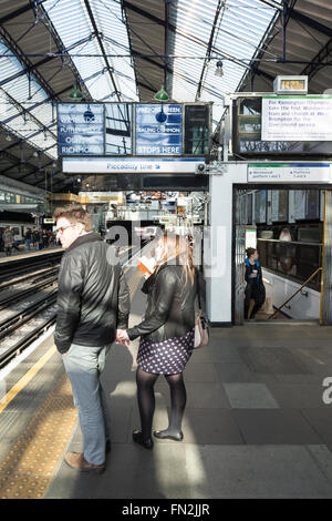 Ein Paar wartet auf einer Plattform in der Londoner U-Bahn Station Earl's Court, Earl's Court, London, England, Vereinigtes Königreich Stockfoto