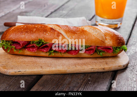 Baguette-Sandwich mit Salami und Kräutern auf einer Holzoberfläche Stockfoto