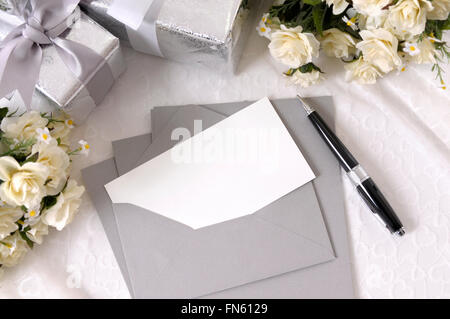 Briefpapier oder Hochzeitseinladung mit Umschlag auf Braut Spitze mit mehreren Hochzeitsgeschenke und weißen Rosensträuße gelegt.  Raum Stockfoto