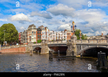 Blick auf Blauwbrug Brücke und typische Häuser im schönen Himmel in Amsterdam, Niederlande. Stockfoto