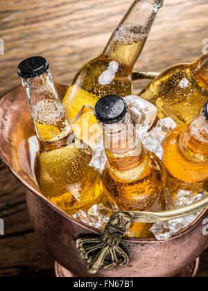 Kalte Flaschen Bier in den ehernen Eimer auf dem Holztisch. Stockfoto