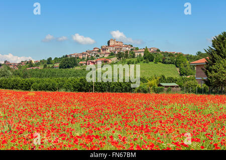 Ländlichen Gebiet der rote Mohn unter blauem Himmel als kleine Stadt auf dem Hügel im Hintergrund im Piemont, Norditalien. Stockfoto