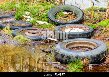 Eine Reihe von gebrauchten alten Autoreifen gelassen in der Natur zu erniedrigen und verschmutzen die Umwelt. Der Boden ist nass und eine Wasserpfütze ist vis Stockfoto