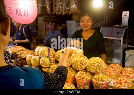 Eine Frau verkauft Popcorn aus Thailand an einen Kunden auf einer Straße Messe in Kampong Cham, Kambodscha. Stockfoto