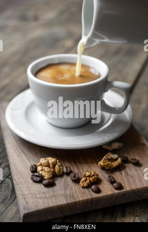 Sahne in einer Tasse Kaffee in eine weiße Tasse gegossen wird. Stockfoto