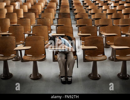 Ein Junge sitzt auf der Vorderseite in einem Saal des leeren Schreibtische, mit seinem Kopf auf seinen Arm. Stockfoto