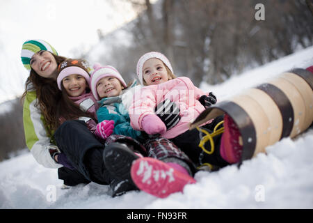 drei Kinder und eine erwachsene Frau sitzt auf einem Schlitten im Schnee. Stockfoto