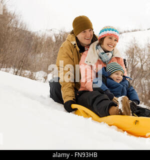 Drei Personen, zwei Erwachsene und ein Kind sitzen auf einem Schlitten auf dem Hügel. Stockfoto