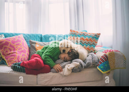 Junge auf Sofa mit golden Retriever Welpe Hund schlafen Stockfoto