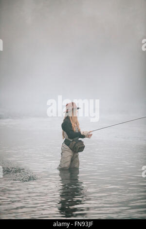 Frau Fischer Fliegen Fischen, stehend in Waders im tiefen Wasser Oberschenkel. Stockfoto