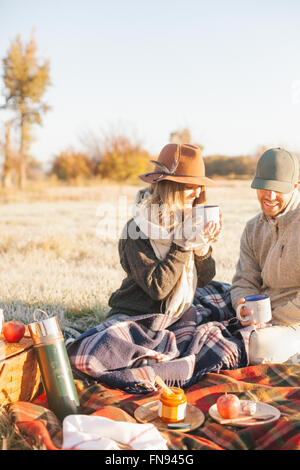 Zwei Menschen, ein paar auf eine Winter-Picknick, sitzen auf einem Tartan Teppich hält heiße Getränke. Stockfoto