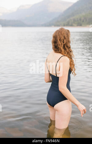 Eine Frau in einem schwarzen Badeanzug waten in einen ruhigen See in den Bergen. Stockfoto