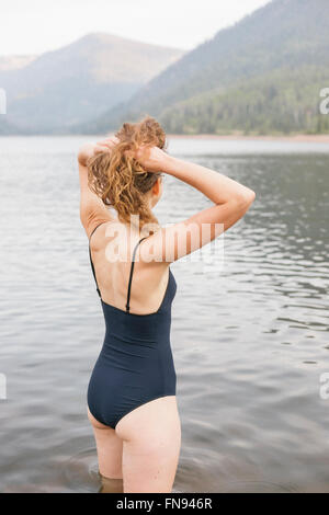 Eine Frau in einem schwarzen Badeanzug waten in einen ruhigen See in den Bergen. Stockfoto