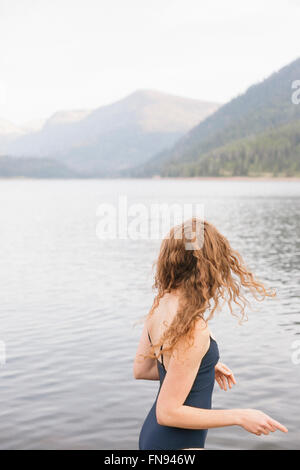Eine Frau in einem schwarzen Badeanzug waten in einen ruhigen See in den Bergen. Stockfoto