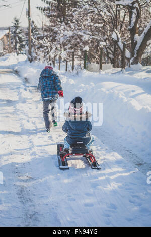 Junge zieht seine Schwester auf einem Schlitten im Schnee Stockfoto