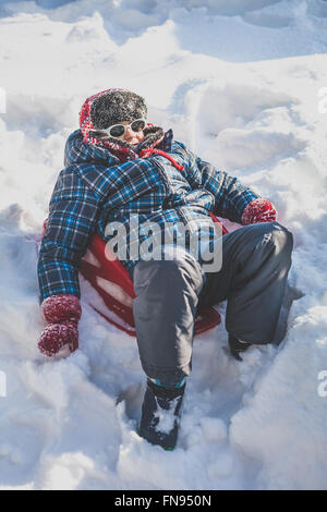 Junge sitzt auf einem Schlitten im Schnee Stockfoto