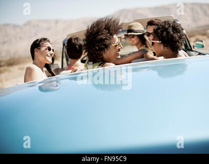 Eine Gruppe von Freunden in einem blassen Blau Cabrio auf offener Straße, fahren durch eine trockene flache Ebene, umgeben von Bergen. Stockfoto