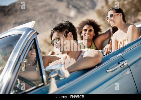 Eine Gruppe von Freunden in einem blassen Blau Cabrio auf offener Straße, fahren durch eine trockene flache Ebene, umgeben von Bergen. Stockfoto