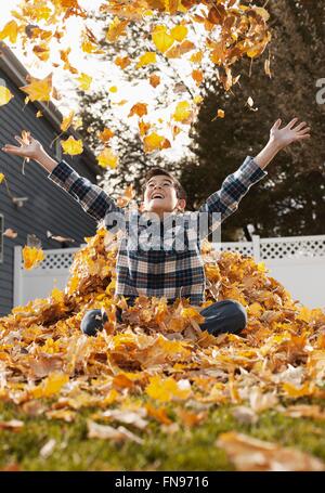 Ein kleiner Junge spielt in einem riesigen Haufen geharkt Herbstlaub. Stockfoto