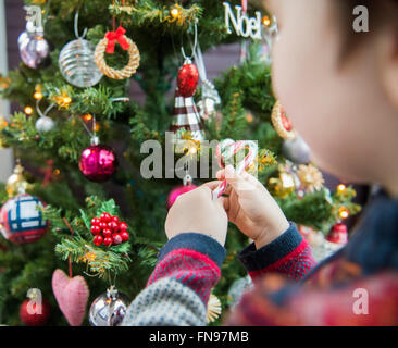 Ein Junge hielt Weihnachtsschmuck und legte sie auf den Baum Stockfoto