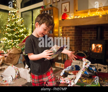 Ein Junge öffnen seine Geschenke am ersten Weihnachtstag das Geschenkpapier zu Boden zu werfen. Stockfoto