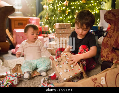 Eine Familie zu Hause am Weihnachtstag, zwei Kinder sitzen unter den Geschenken vom Baum. Stockfoto