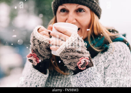 Frau im Schnee hält heißes Getränk Stockfoto
