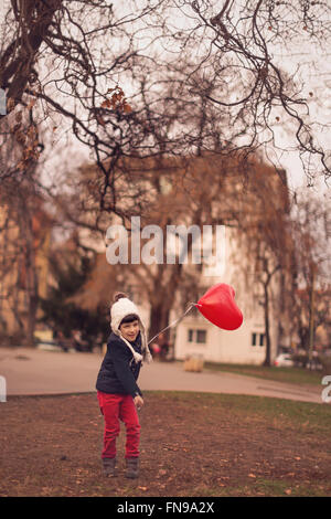 Kleiner Junge spielt mit herzförmigen roten Ballon Stockfoto