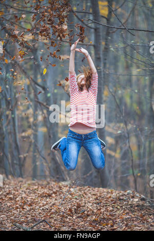 Mitte Erwachsene Frau springt in die Luft im Wald Stockfoto