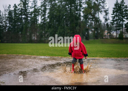 Junge, springen in eine Pfütze im Regen Stockfoto