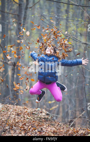 Mädchen, springen und werfen im Herbst Blätter in der Luft Stockfoto